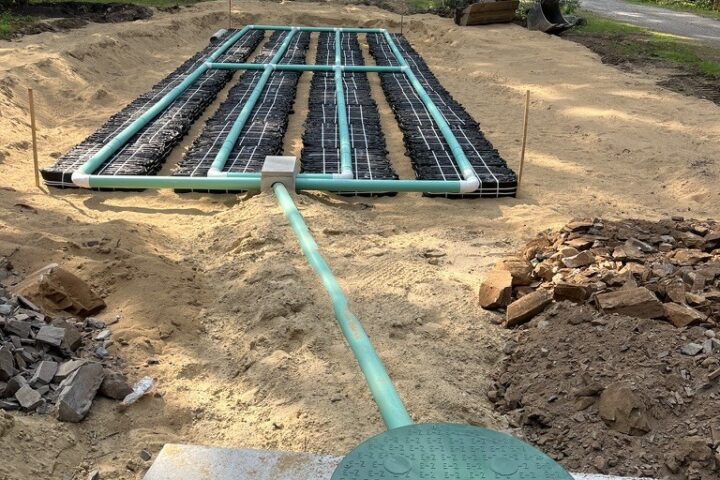 Newly installed septic system with the concrete tank lid and riser in the foreground and the leach field chambers bedded in sand behind.