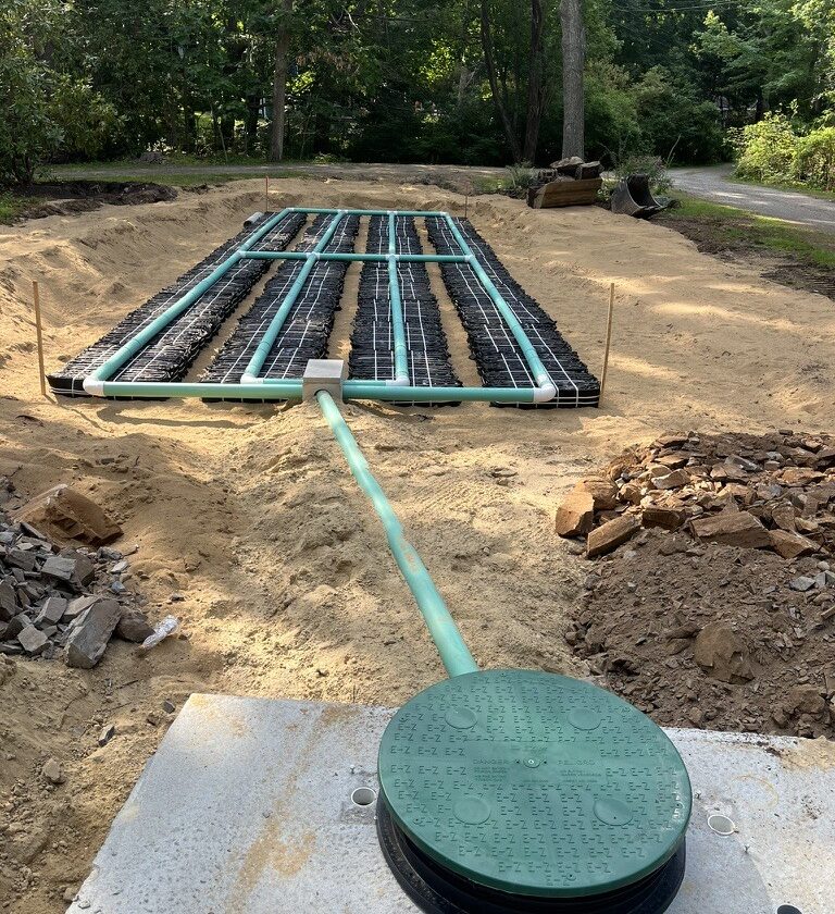 Newly installed septic system with the concrete tank lid and riser in the foreground and the leach field chambers bedded in sand behind.