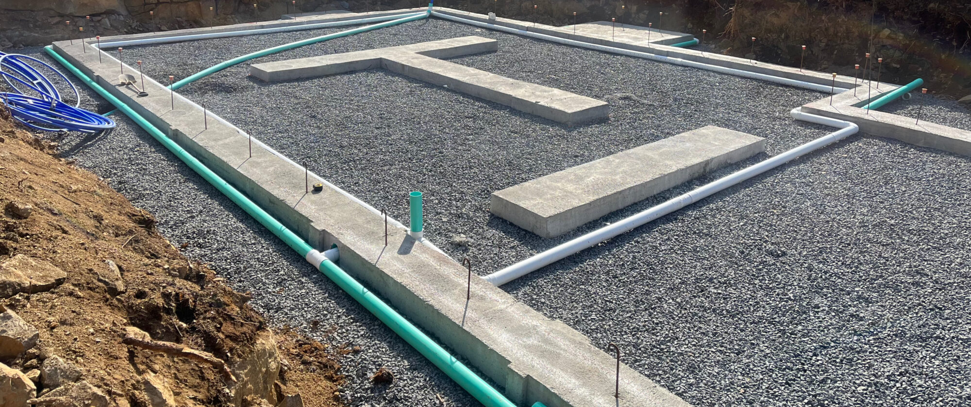 Foundation excavation cut to ledge, with poured concrete footings, a compacted gravel base and under-slab drain and water lines run before the slab is poured.