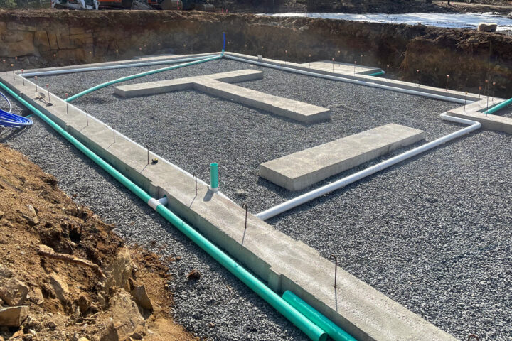 Foundation excavation cut to ledge, with poured concrete footings, a compacted gravel base and under-slab drain and water lines run before the slab is poured.